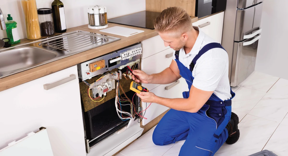 Technician using a multimeter to test an open dishwasher control panel