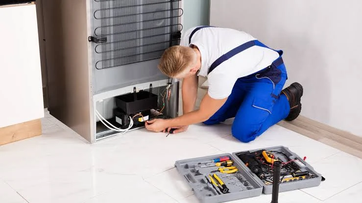 Technician checking compressor components behind a refrigerator