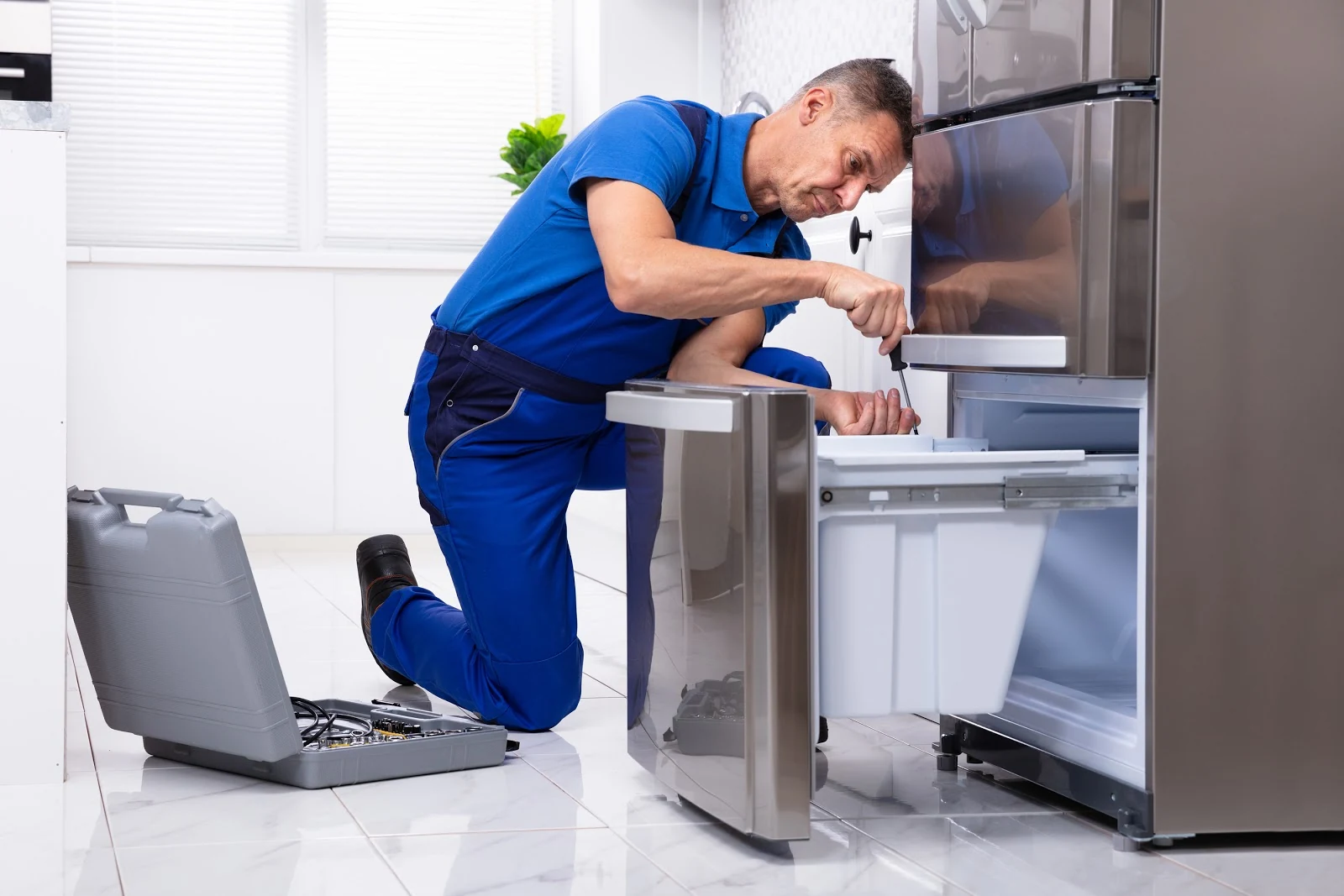 Technician repairing an open refrigerator drawer in a bright home kitchen