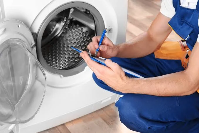 Technician writing assessment notes beside an open front-loading washing machine
