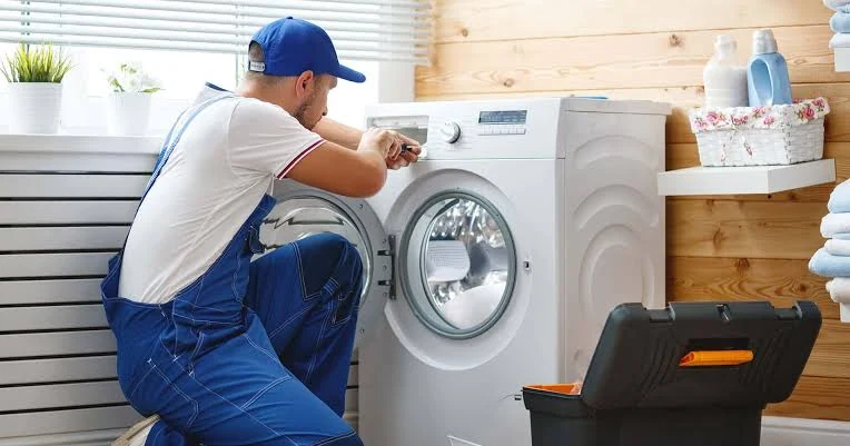 Technician repairing washing-machine controls in a sunny laundry room